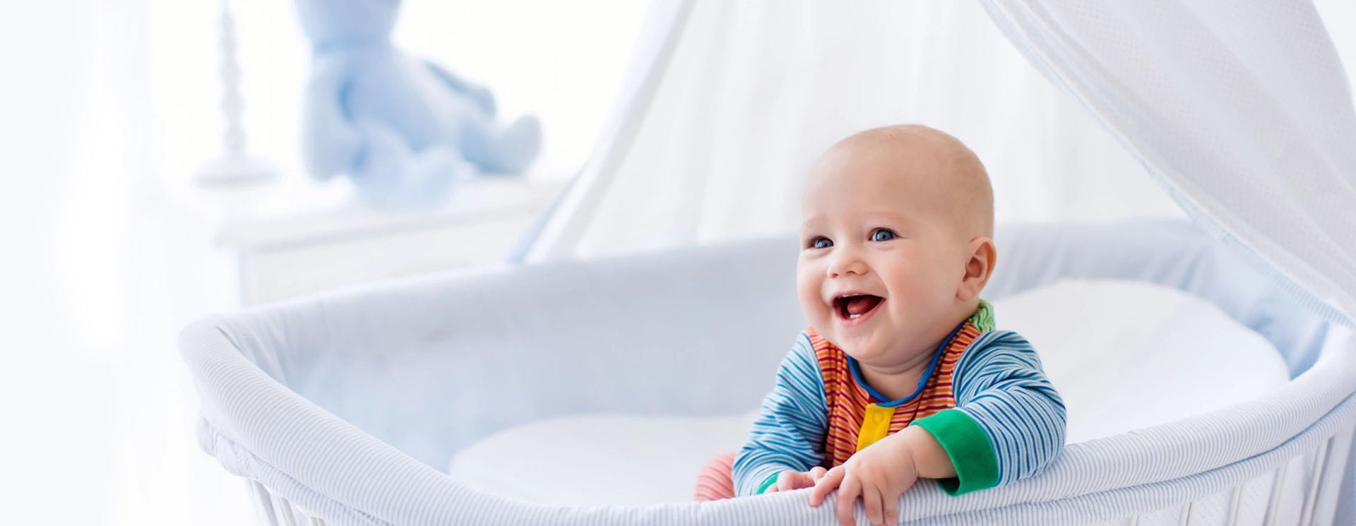 A baby is smiling while sitting in his crib.