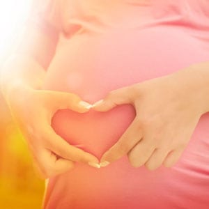 A woman holding her stomach in the shape of a heart.